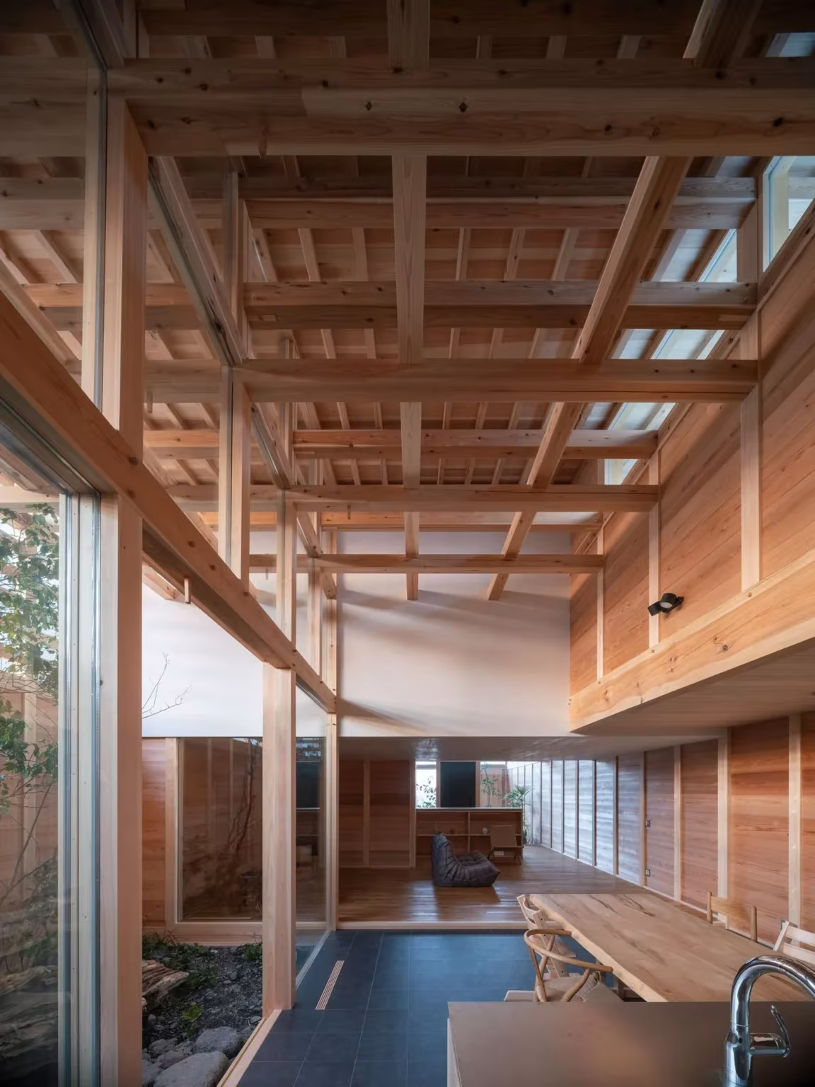 Entramado de cedro del techo, ventanal y mesa de comedor al fondo en la casa en Aichi, Japón