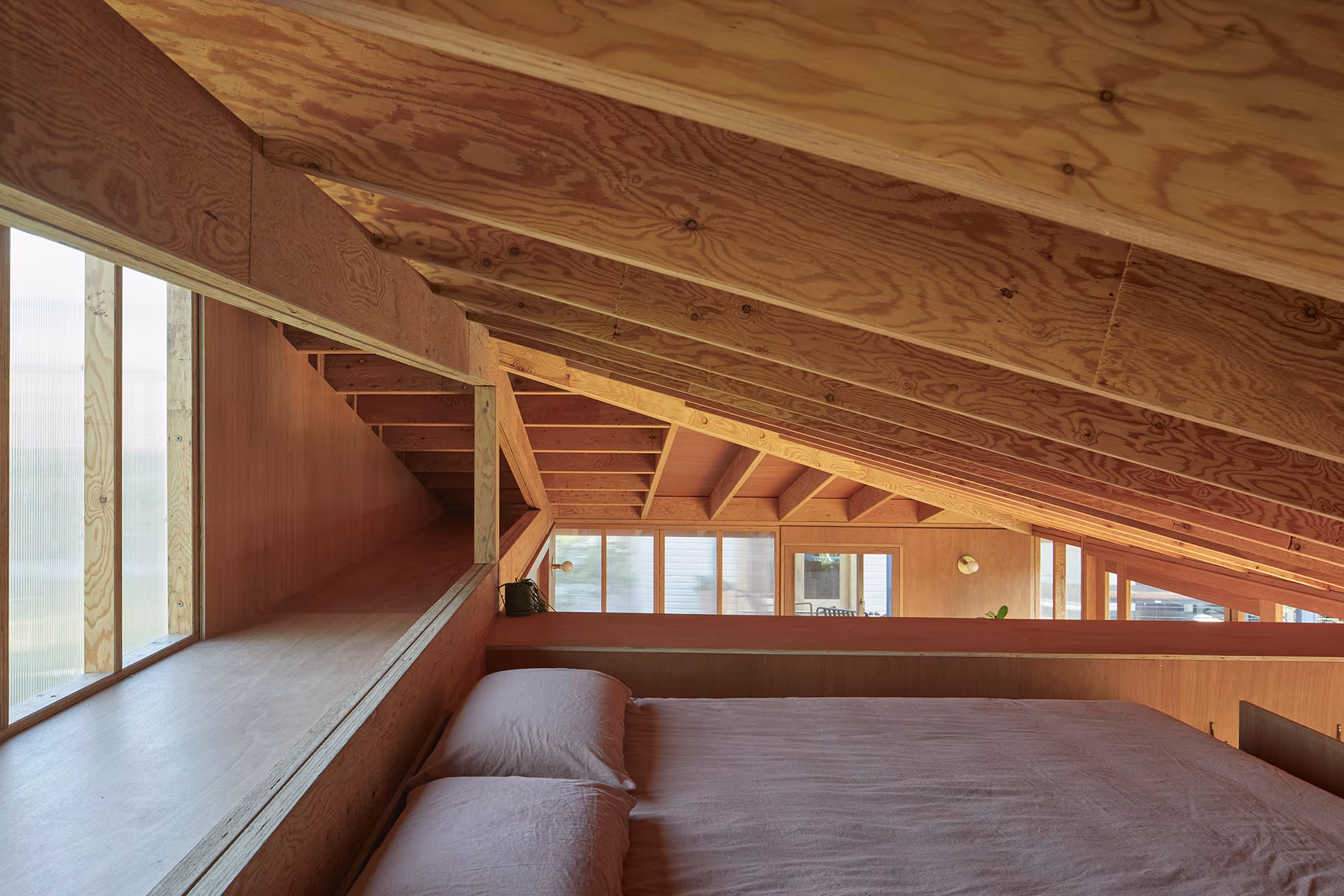 Dormitorio en altillo bajo la cubierta de vigas de madera con ventana corrida en Princes Studio, Curious Practice