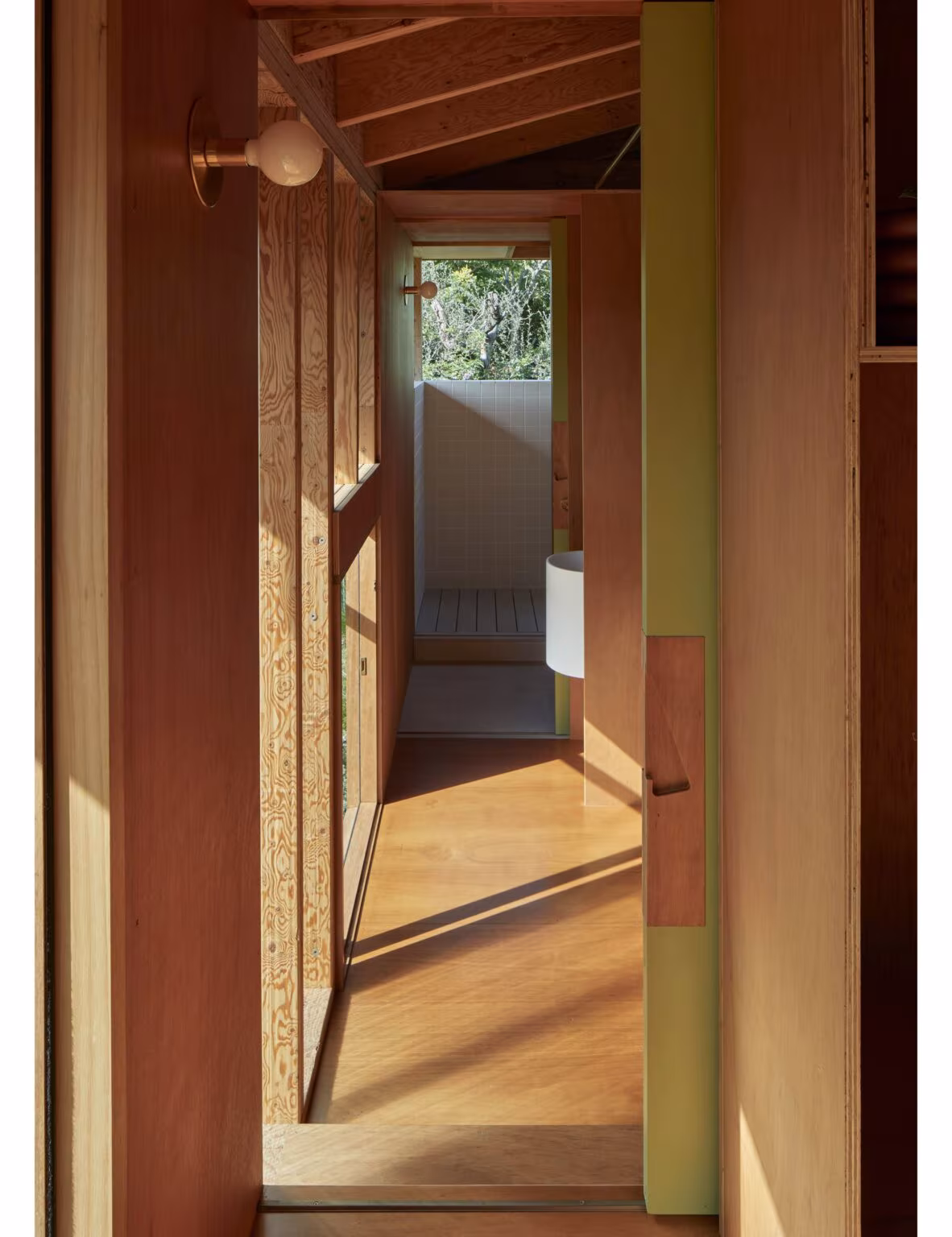 Pasillo estrecho de madera con paneles verdes y puerta abierta al baño en Princes Studio de Curious Practice