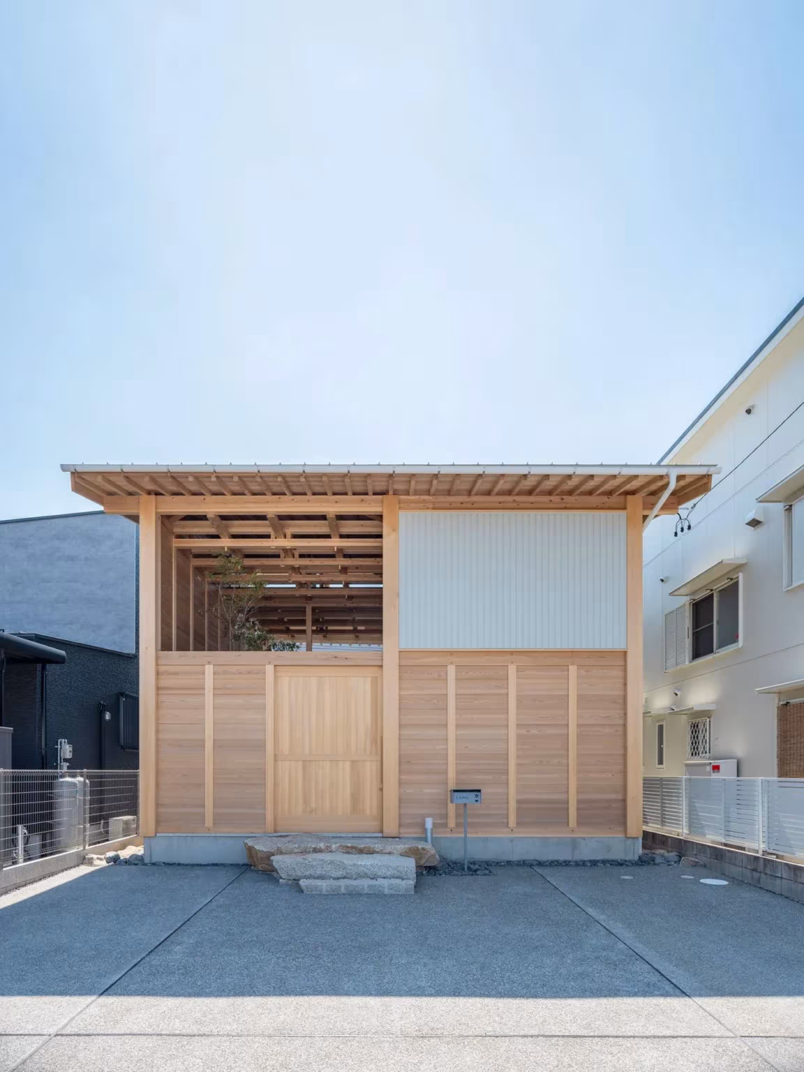 Casa en Aichi de Ryota Sekiya con entrada de madera y frente de enrejado de cedro sobre el patio de hormigón