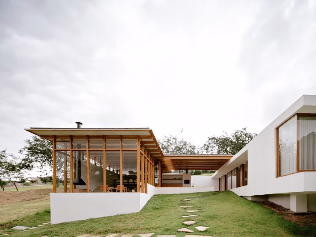 Casa de una planta con muros blancos y pabellón de madera y vidrio sobre una pradera verde