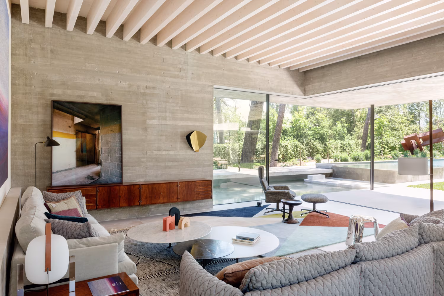 Salón abierto al jardín con vigas de madera claras, hormigón visto y esquina de vidrio en el Proyecto AS