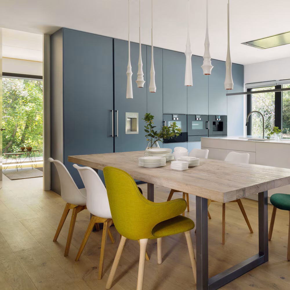 Kitchen with blue cabinets, an island, and a wooden table with yellow and green chairs in the CH Project
