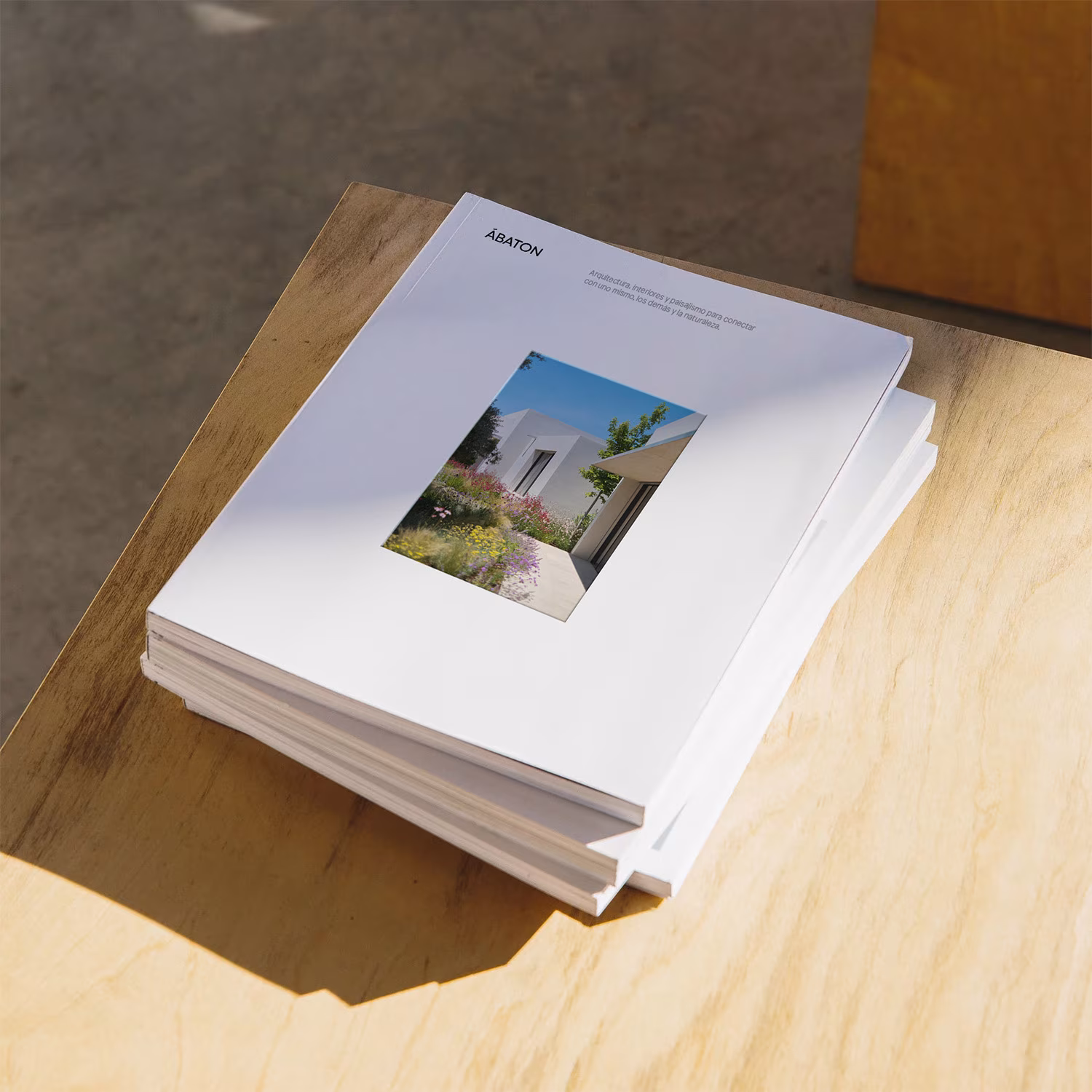 Libro de proyectos de Ábaton sobre una mesa de madera con una vivienda blanca en la portada